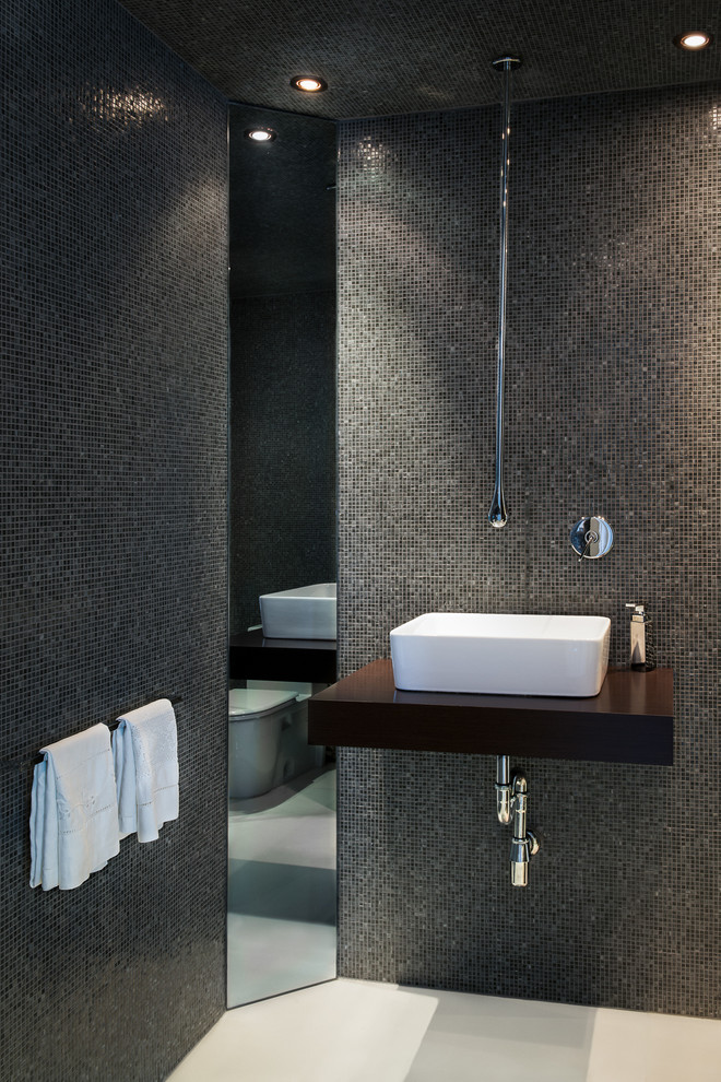 Modern inredning av ett mellanstort badrum med dusch, med öppna hyllor, skåp i mellenmörkt trä, en toalettstol med hel cisternkåpa, grå kakel, mosaik, svarta väggar, betonggolv, ett fristående handfat och träbänkskiva