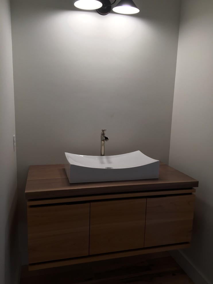 Idée de décoration pour une salle d'eau design en bois foncé de taille moyenne avec un placard à porte plane, un mur gris, une vasque et un plan de toilette en bois.