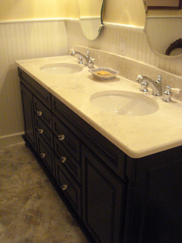 Inredning av ett klassiskt badrum, med ett undermonterad handfat, luckor med upphöjd panel, svarta skåp, bänkskiva i kvarts, gula väggar och klinkergolv i keramik