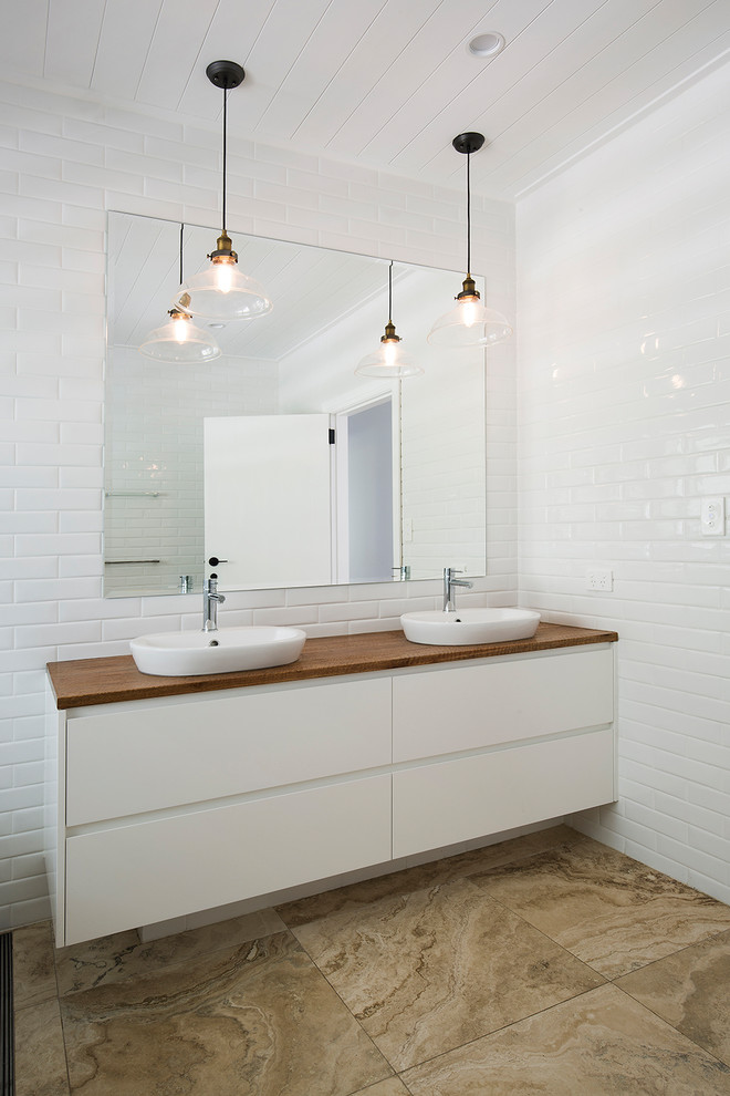 Modelo de cuarto de baño actual con armarios con paneles lisos, puertas de armario blancas, baldosas y/o azulejos de cemento, aseo y ducha, lavabo sobreencimera, encimera de madera y suelo marrón