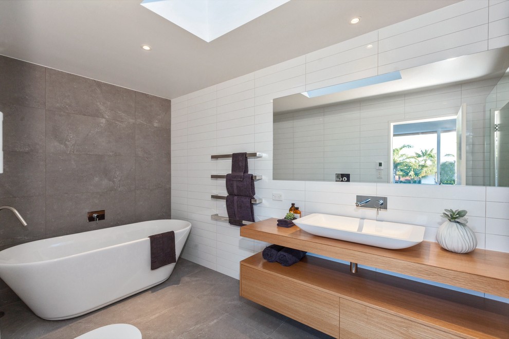 Contemporary ensuite bathroom in Auckland with a vessel sink, flat-panel cabinets, light wood cabinets, wooden worktops, a freestanding bath, white tiles, concrete flooring and brown worktops.