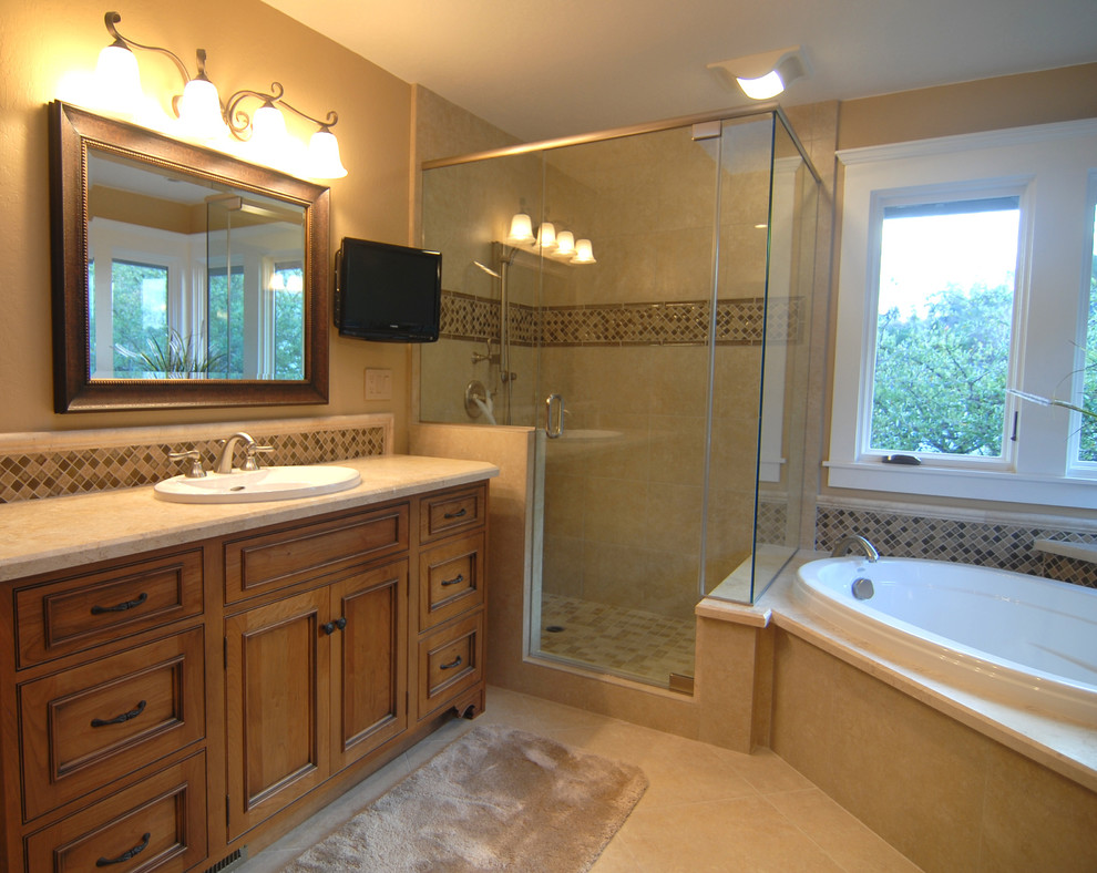 Inredning av ett klassiskt en-suite badrum, med ett nedsänkt handfat, luckor med profilerade fronter, skåp i mellenmörkt trä, bänkskiva i kalksten, ett platsbyggt badkar, en hörndusch, flerfärgad kakel, gula väggar och travertin golv
