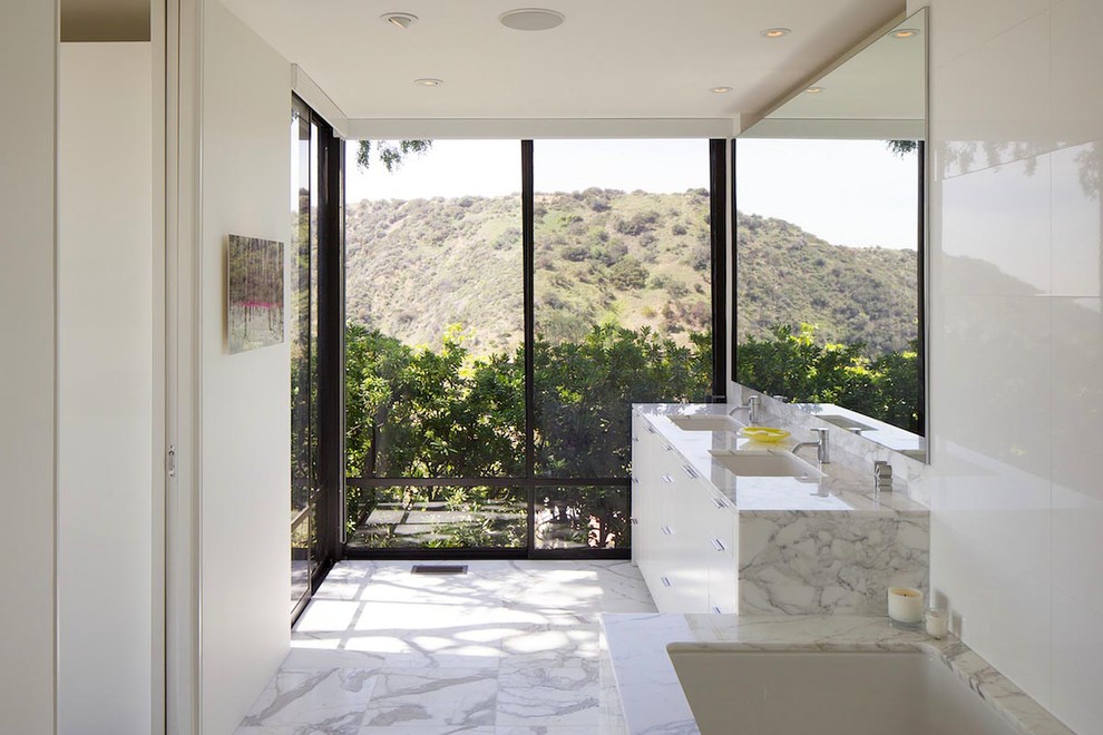 Cette image montre une salle de bain design avec un lavabo encastré, un placard à porte plane, des portes de placard blanches, une baignoire encastrée et un carrelage blanc.