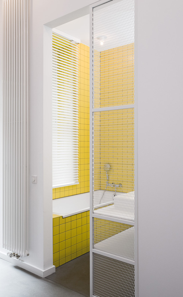 Aménagement d'une petite salle de bain principale contemporaine avec un placard sans porte, des portes de placard blanches, une baignoire posée, un combiné douche/baignoire, un carrelage jaune, mosaïque, un mur jaune, sol en béton ciré, une vasque et un sol gris.