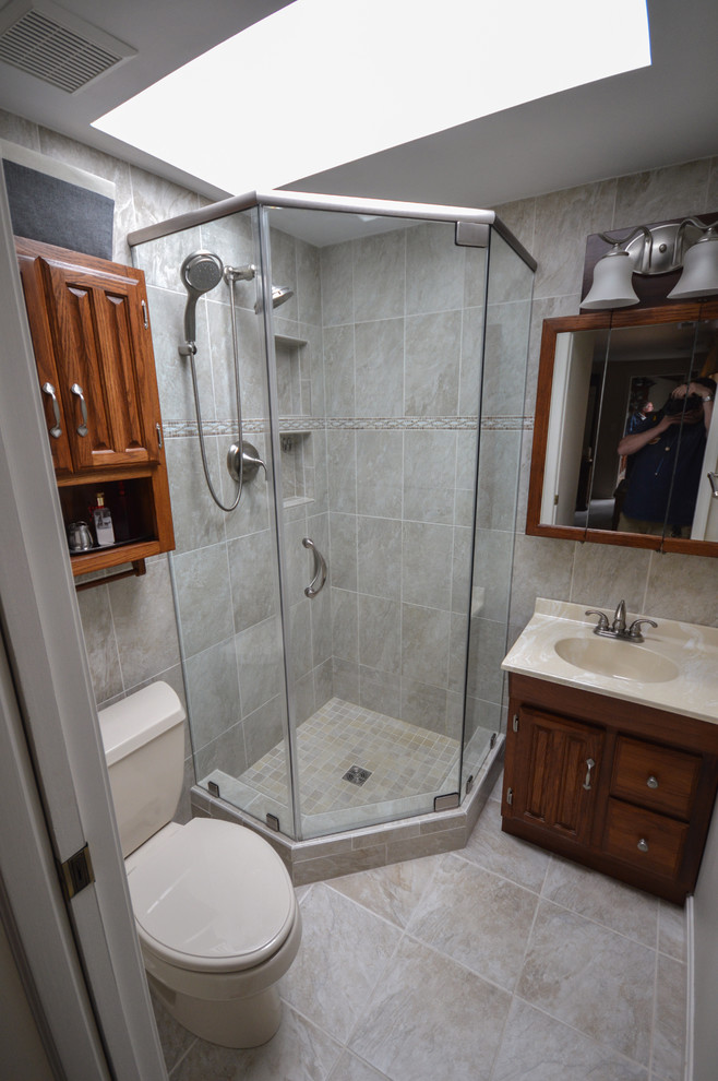 Modelo de cuarto de baño principal de estilo americano pequeño con lavabo integrado, armarios con paneles con relieve, puertas de armario de madera oscura, encimera de acrílico, ducha esquinera y sanitario de una pieza