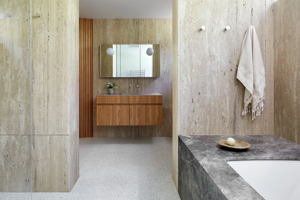 Design ideas for a large contemporary ensuite bathroom in Melbourne with flat-panel cabinets, brown cabinets, a built-in bath, a walk-in shower, a one-piece toilet, beige tiles, travertine tiles, beige walls, terrazzo flooring, a submerged sink, limestone worktops, multi-coloured floors, an open shower, grey worktops, a single sink and a floating vanity unit.
