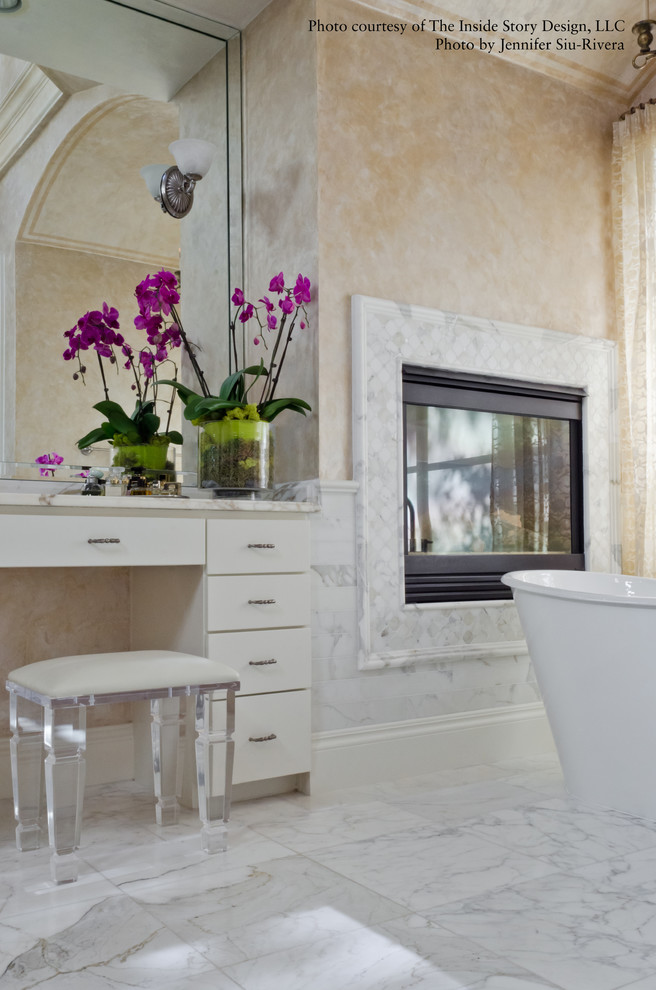 Foto på ett stort vintage vit en-suite badrum, med släta luckor, vita skåp, ett fristående badkar, vit kakel, marmorkakel, beige väggar, marmorgolv, ett undermonterad handfat, marmorbänkskiva och vitt golv