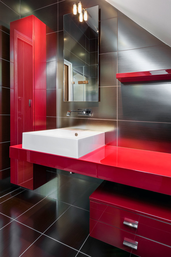 Cette photo montre une petite salle de bain principale tendance avec un placard à porte plane, des portes de placard rouges, un carrelage gris, des carreaux de céramique, un mur gris, un sol en carrelage de céramique, une vasque et un plan de toilette en verre.