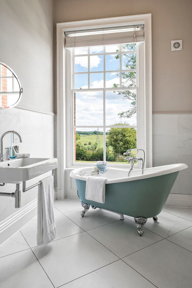 Foto de cuarto de baño principal tradicional renovado pequeño con bañera con patas, baldosas y/o azulejos blancos, paredes beige, suelo de baldosas de porcelana y lavabo suspendido