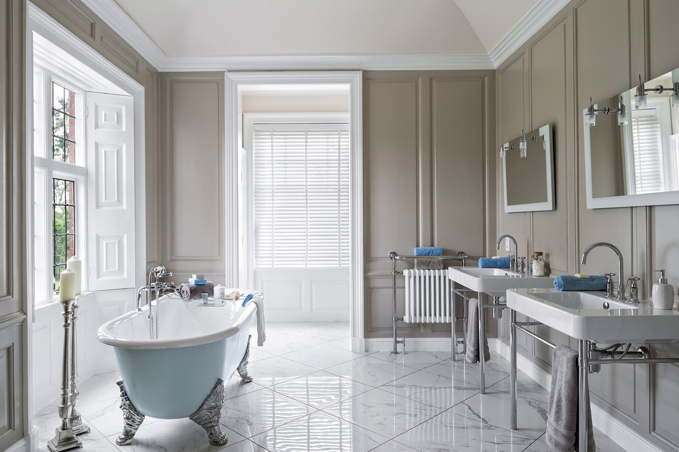 Large elegant master white tile marble floor claw-foot bathtub photo in Hampshire with brown walls, a console sink and open cabinets