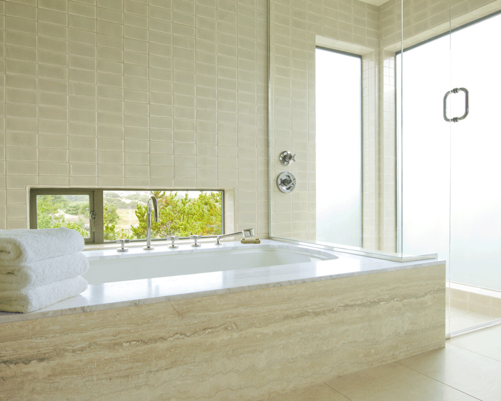 Exemple d'une salle de bain avec une baignoire encastrée, un carrelage beige, du carrelage en travertin et une fenêtre.