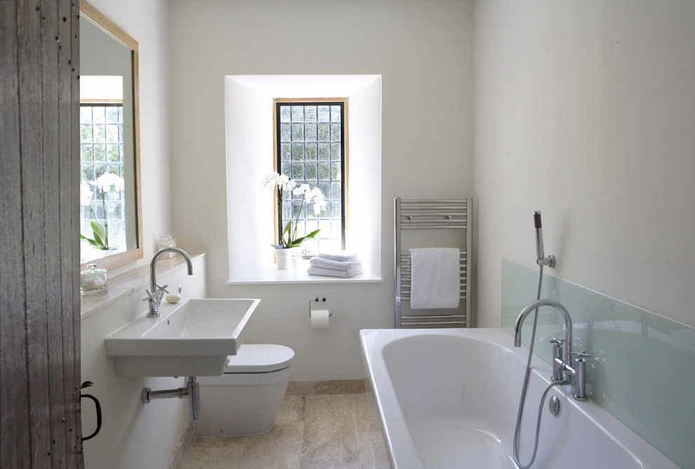 Modern inredning av ett litet badrum, med ett fristående badkar, en öppen dusch, en vägghängd toalettstol, beige kakel, stenkakel, beige väggar, kalkstensgolv, ett väggmonterat handfat och träbänkskiva