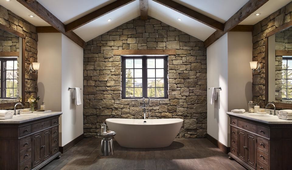Rustik inredning av ett stort badrum, med luckor med profilerade fronter, skåp i mörkt trä, ett fristående badkar, brun kakel, stenkakel, vita väggar, mörkt trägolv, ett undermonterad handfat, bänkskiva i kalksten och brunt golv