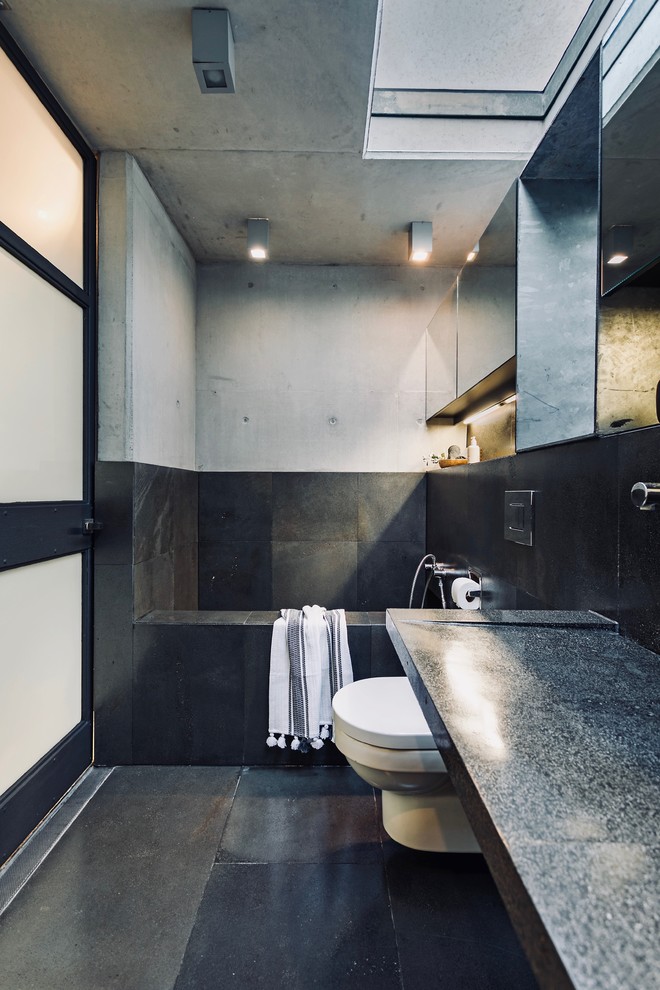Exemple d'une salle de bain principale moderne de taille moyenne avec un placard à porte vitrée, WC suspendus, un carrelage noir, un carrelage de pierre, un mur noir, un lavabo intégré, un plan de toilette en terrazzo, un sol noir et un plan de toilette gris.