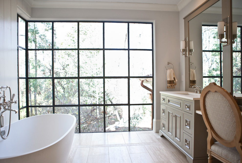 Cette image montre une grande salle de bain principale design avec un placard à porte affleurante, des portes de placard beiges, une baignoire indépendante, un sol en carrelage de porcelaine, un lavabo encastré, un plan de toilette en surface solide, un sol beige et un mur gris.