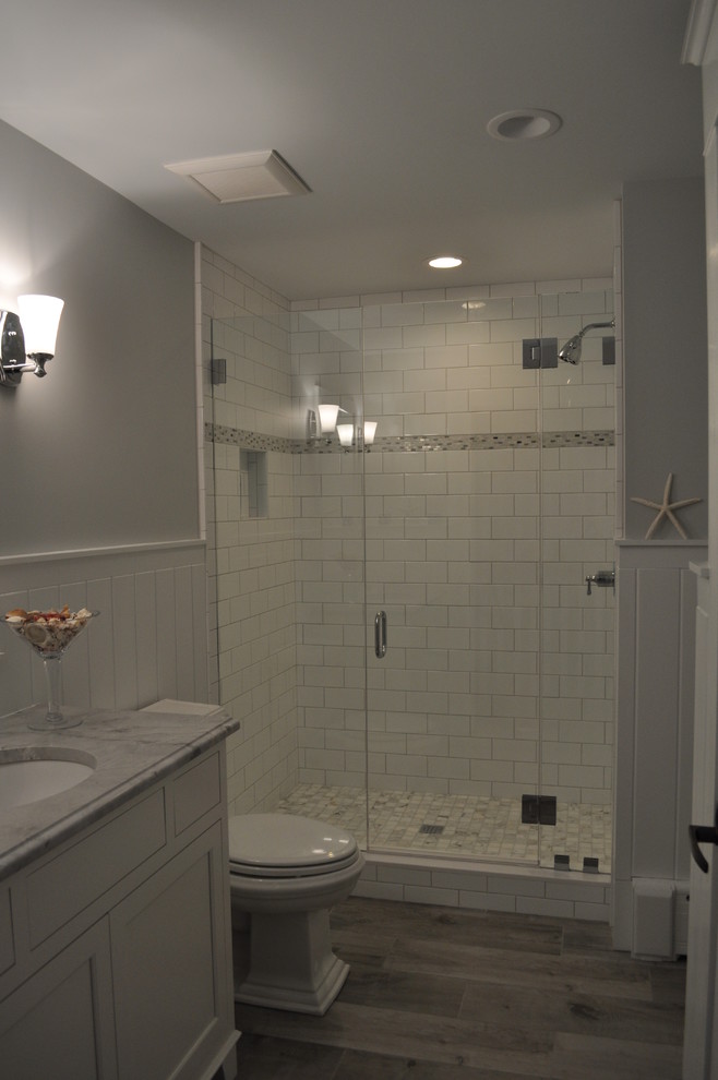 Modern inredning av ett mellanstort badrum med dusch, med luckor med infälld panel, vita skåp, en dusch i en alkov, en toalettstol med separat cisternkåpa, vit kakel, tunnelbanekakel, grå väggar, plywoodgolv, ett undermonterad handfat och marmorbänkskiva
