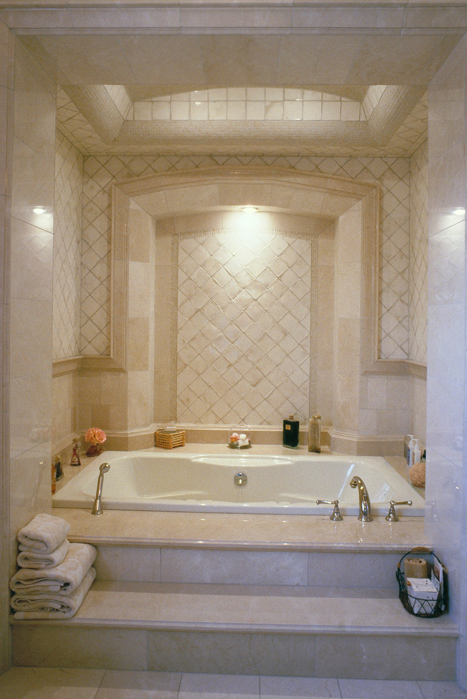 Klassisk inredning av ett badrum, med beige skåp, ett badkar i en alkov, beige kakel, keramikplattor, beige väggar, ett undermonterad handfat och kaklad bänkskiva
