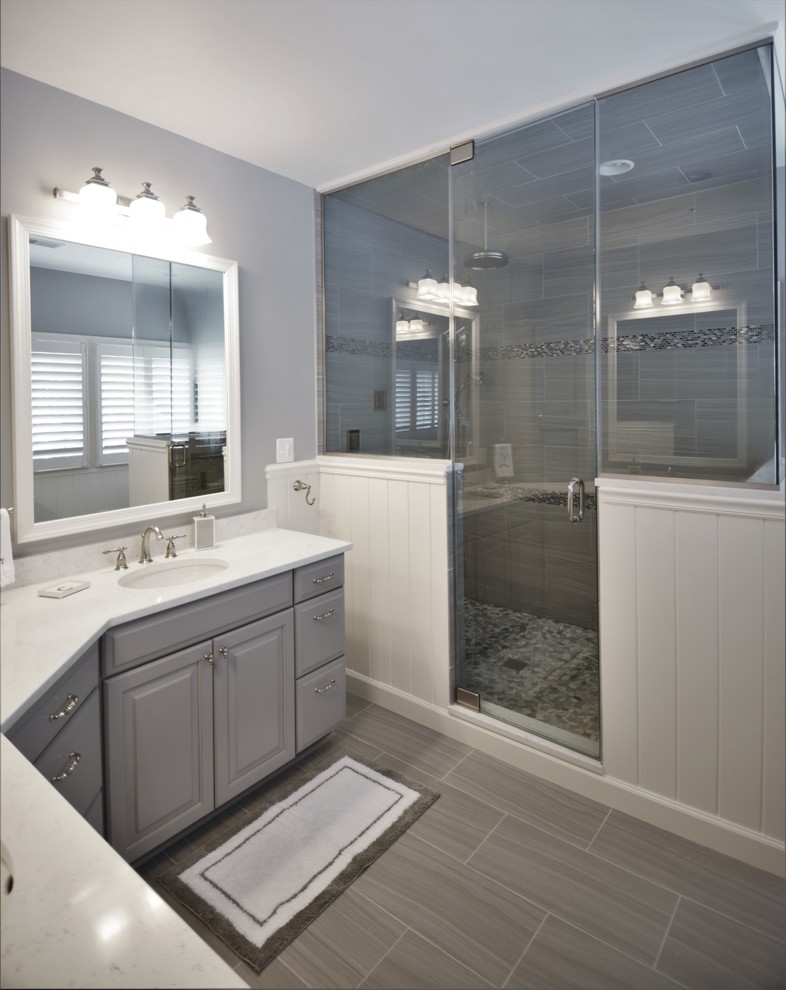 Exemple d'une grande salle de bain tendance avec un placard avec porte à panneau surélevé, des portes de placard grises, un carrelage gris, des carreaux de porcelaine, un mur gris, un sol en carrelage de porcelaine, un lavabo encastré et un plan de toilette en quartz modifié.