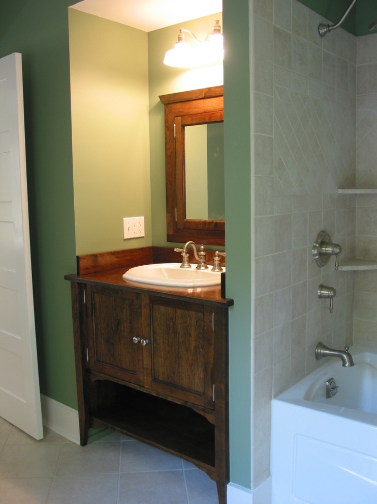 Cette image montre une salle de bain principale traditionnelle en bois foncé avec un lavabo posé, un placard avec porte à panneau encastré, un plan de toilette en bois, une baignoire en alcôve, un combiné douche/baignoire, WC séparés, un carrelage beige, des carreaux de porcelaine, un mur vert et un sol en carrelage de porcelaine.