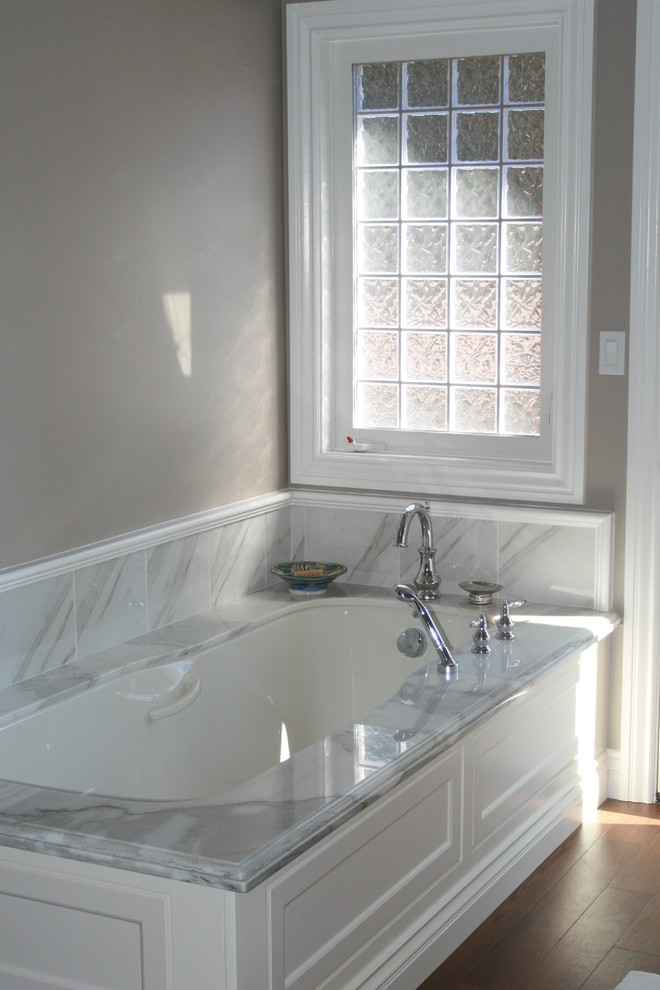 Modelo de cuarto de baño tradicional con bañera encastrada, baldosas y/o azulejos de piedra, paredes grises y suelo de madera en tonos medios