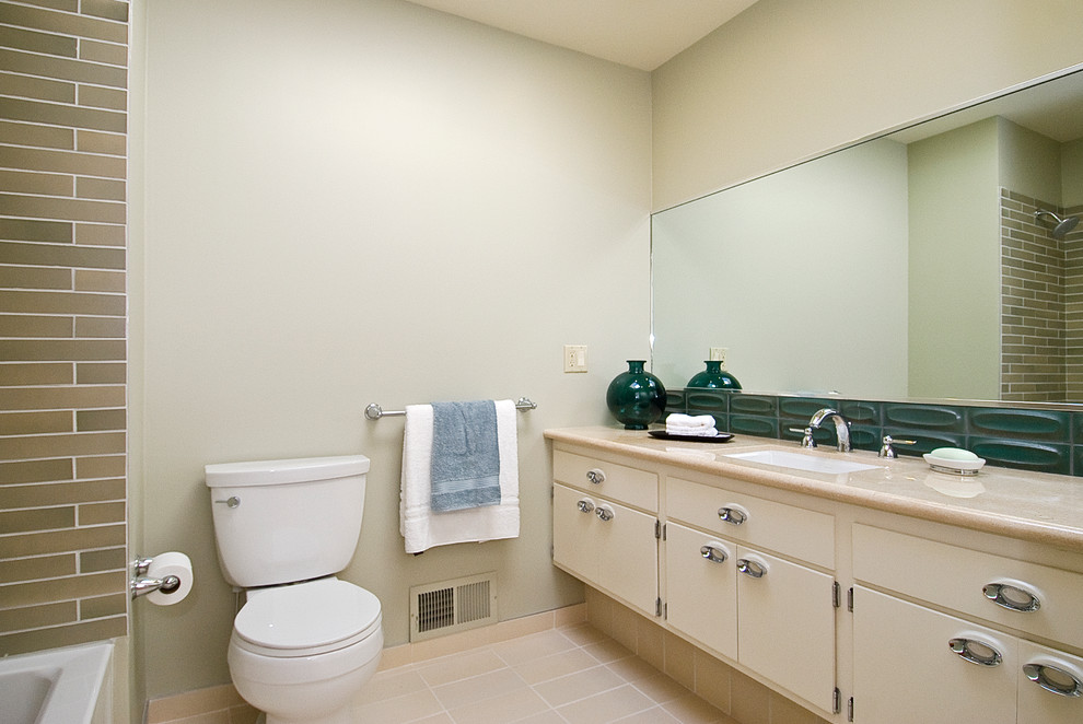Bild på ett funkis en-suite badrum, med släta luckor, beige skåp, ett platsbyggt badkar, en dusch/badkar-kombination, en toalettstol med separat cisternkåpa, blå kakel, porslinskakel, beige väggar, klinkergolv i keramik, ett väggmonterat handfat och granitbänkskiva