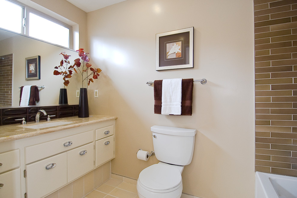 Modern inredning av ett en-suite badrum, med släta luckor, en dusch/badkar-kombination, en toalettstol med separat cisternkåpa, klinkergolv i keramik, vita skåp, ett undermonterat badkar, brun kakel, keramikplattor, vita väggar, ett nedsänkt handfat och granitbänkskiva