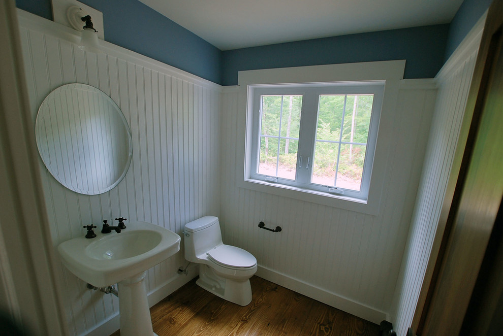Foto på ett litet lantligt badrum, med ett piedestal handfat, en toalettstol med hel cisternkåpa, vita väggar och mellanmörkt trägolv