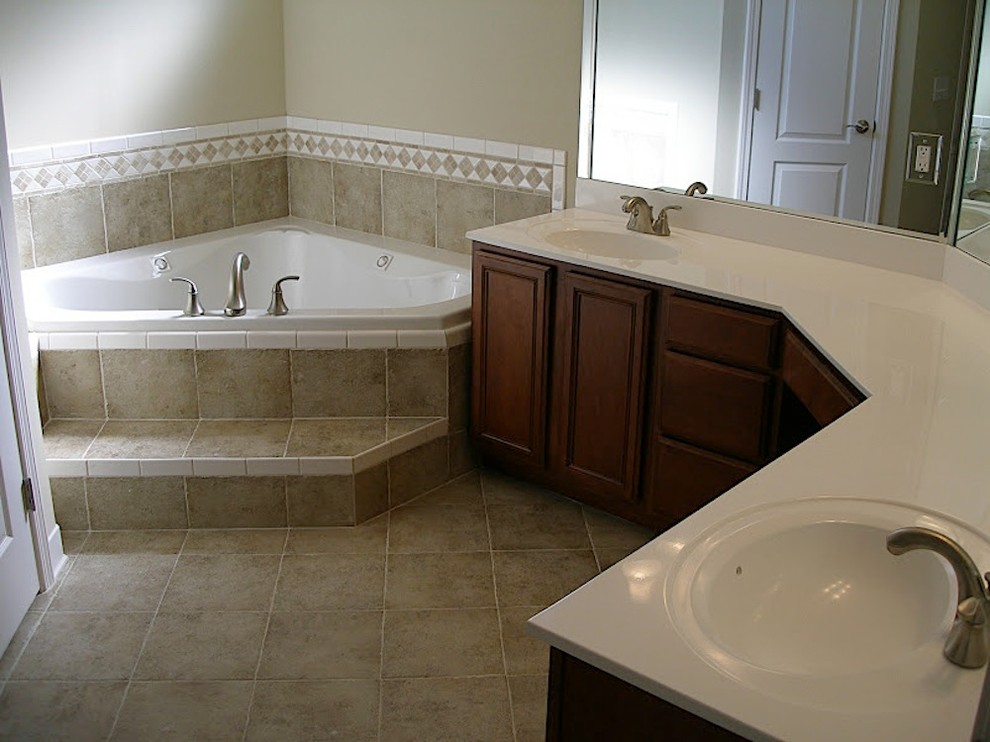 Photo of a medium sized traditional ensuite bathroom in Jacksonville with raised-panel cabinets, dark wood cabinets, a corner bath, brown tiles, porcelain tiles, beige walls, porcelain flooring, an integrated sink, solid surface worktops, brown floors and white worktops.