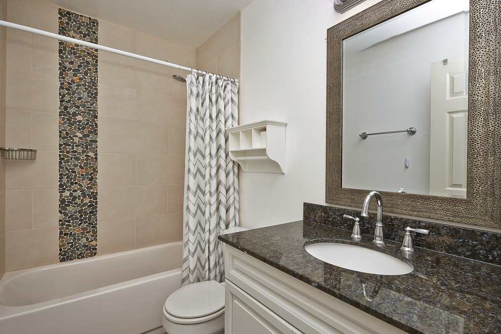 Стильный дизайн: ванная комната среднего размера в современном стиле с монолитной раковиной, ванной в нише, душем над ванной, унитазом-моноблоком, бежевой плиткой, каменной плиткой, плоскими фасадами, белыми фасадами, столешницей из гранита и белыми стенами - последний тренд