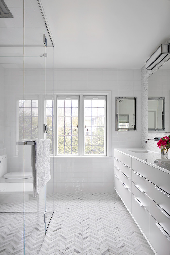 Photo of a contemporary bathroom in New York with flat-panel cabinets, grey cabinets, a built-in shower, white tiles, a submerged sink, marble worktops, a one-piece toilet and metro tiles.
