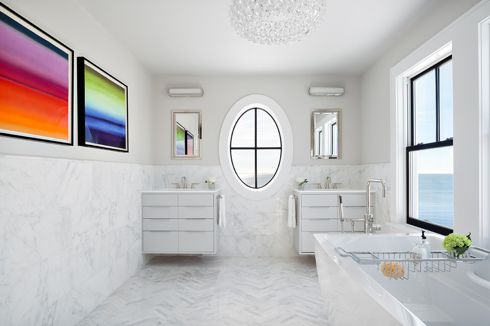 Cette photo montre une salle de bain tendance avec un placard à porte plane, des portes de placard blanches, un carrelage blanc, un carrelage de pierre, un mur blanc et un sol en marbre.