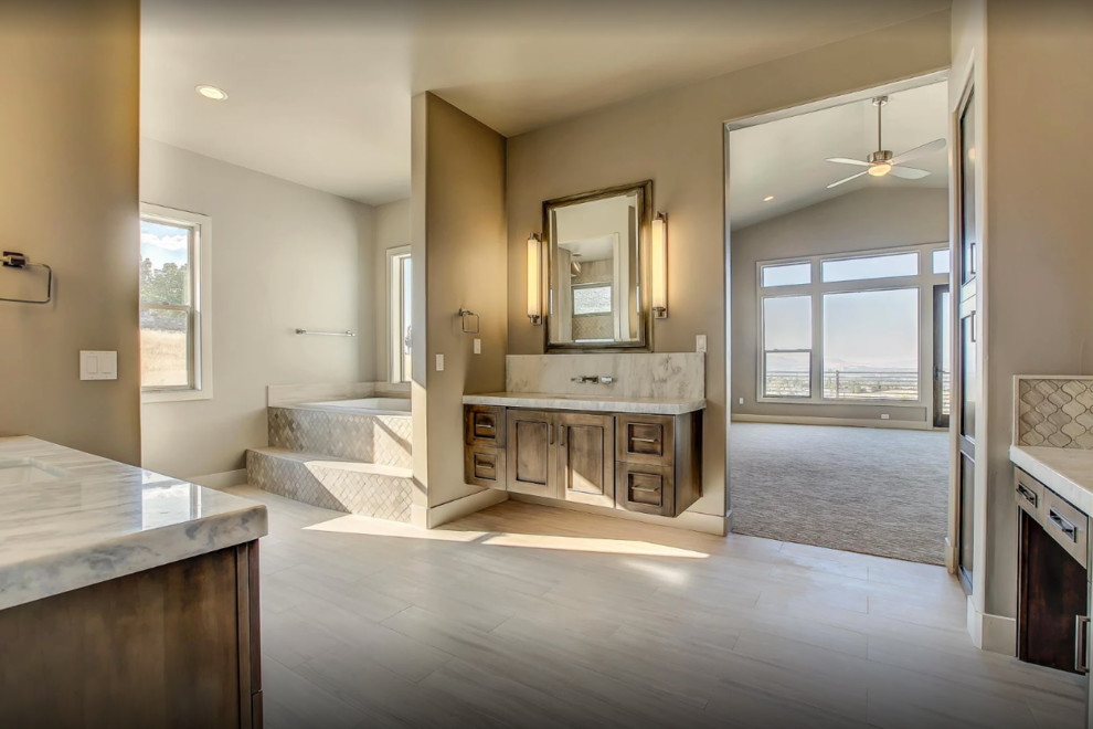 Large transitional master porcelain tile and beige floor drop-in bathtub photo in Other with recessed-panel cabinets, dark wood cabinets, a two-piece toilet, gray walls, an undermount sink and marble countertops