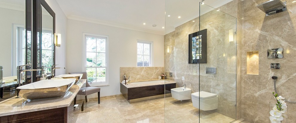 This is an example of an expansive family bathroom in London with dark wood cabinets, a built-in bath, a built-in shower, a wall mounted toilet, beige tiles, beige walls, ceramic flooring, a vessel sink and marble worktops.