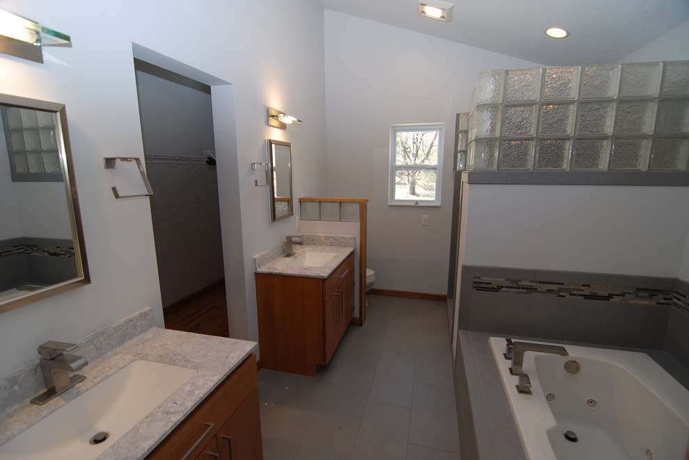 Cette photo montre une grande salle de bain moderne en bois brun avec un sol en carrelage de céramique, un lavabo posé, un plan de toilette en carrelage, un placard à porte plane, une baignoire posée, une douche ouverte, un carrelage gris et un mur gris.