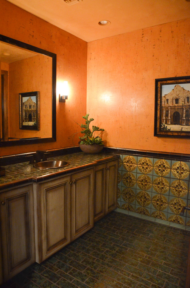 Cette photo montre une salle de bain sud-ouest américain en bois vieilli avec un placard avec porte à panneau encastré, un mur orange, un sol en carrelage de céramique, un lavabo posé et un plan de toilette en granite.