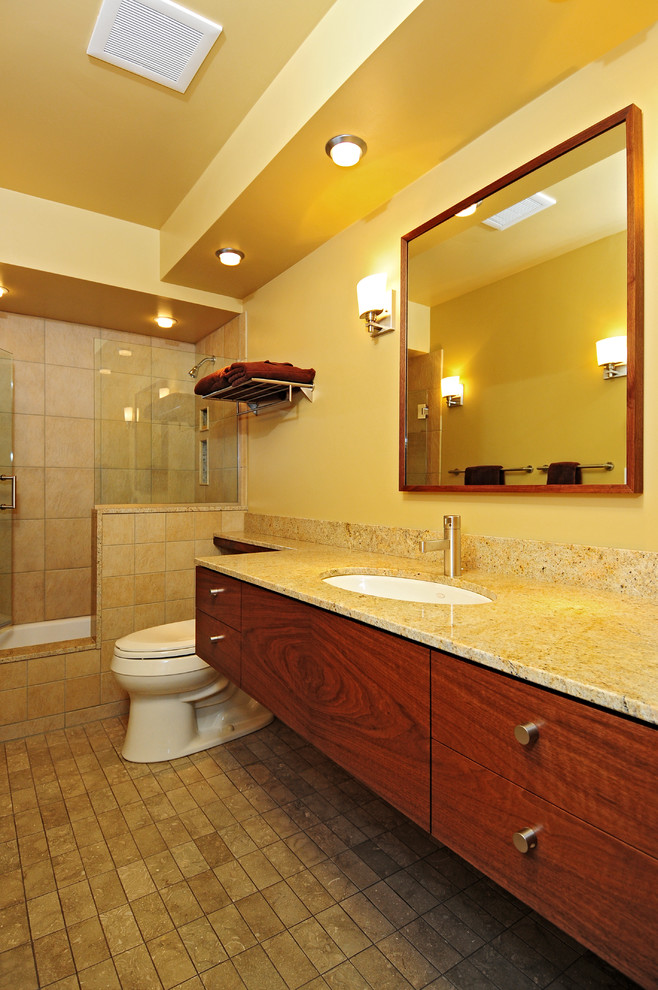 Contemporary ensuite bathroom in Seattle with a submerged sink, flat-panel cabinets, medium wood cabinets, granite worktops, an alcove bath, a shower/bath combination, a two-piece toilet, beige tiles, stone tiles, beige walls and limestone flooring.