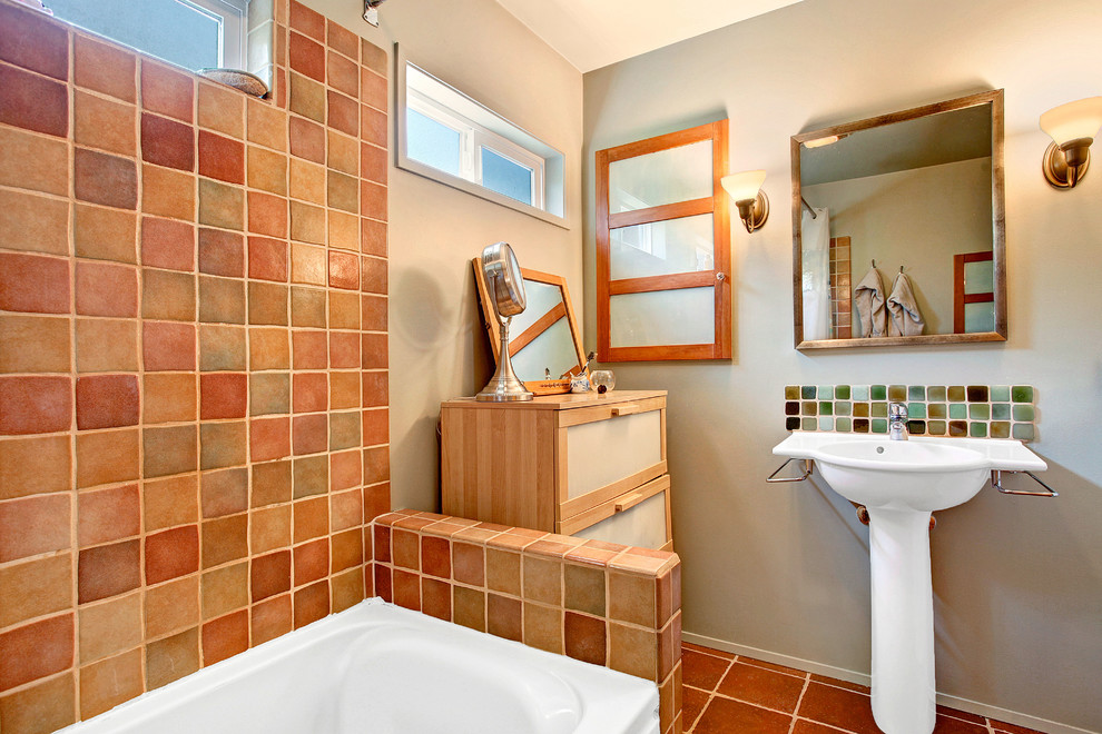Foto på ett eklektiskt badrum, med ett piedestal handfat, möbel-liknande, skåp i ljust trä, ett badkar i en alkov, en dusch/badkar-kombination, en toalettstol med separat cisternkåpa, flerfärgad kakel, keramikplattor, grå väggar och klinkergolv i keramik
