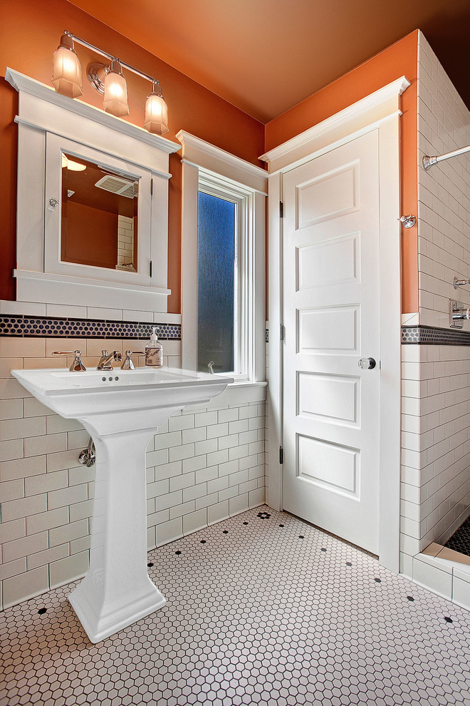 Amerikansk inredning av ett badrum med dusch, med ett piedestal handfat, en dusch i en alkov, en toalettstol med separat cisternkåpa, vit kakel, keramikplattor, orange väggar och klinkergolv i keramik