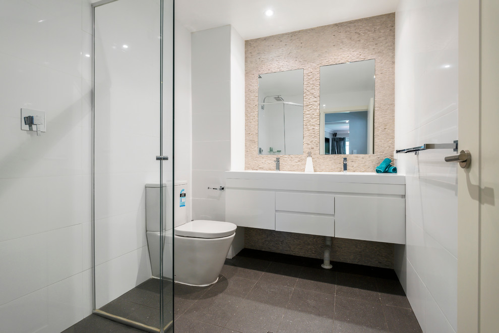 Diseño de cuarto de baño actual pequeño con ducha esquinera, sanitario de una pieza, baldosas y/o azulejos grises, paredes blancas, aseo y ducha y lavabo suspendido