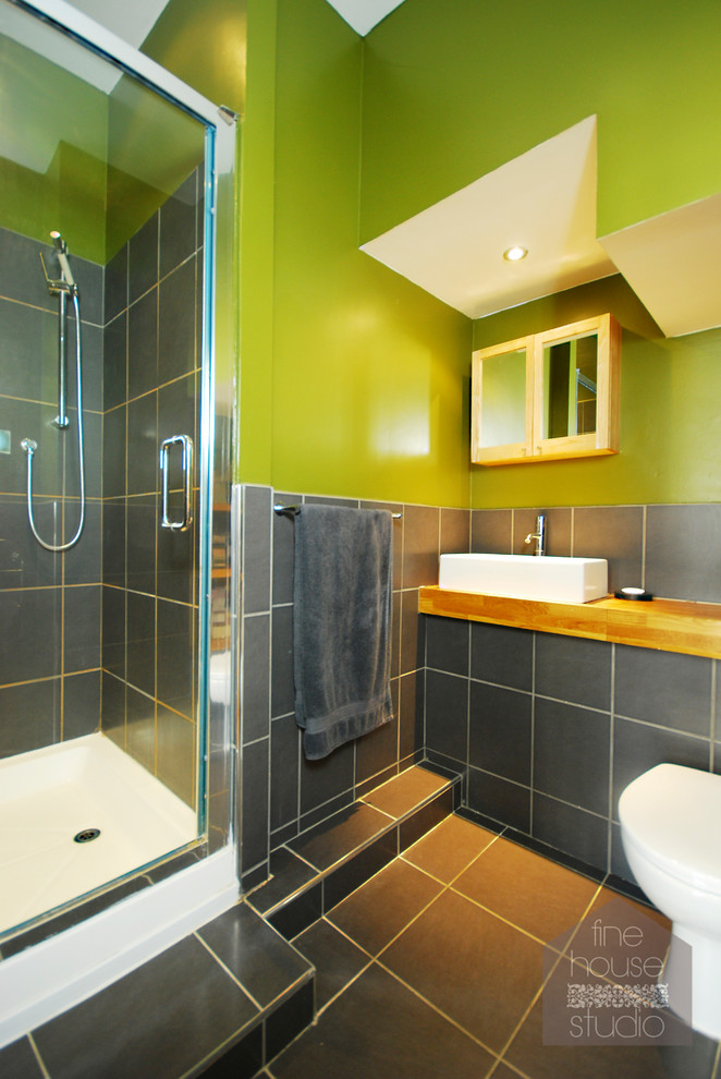 Modern inredning av ett litet badrum med dusch, med ett fristående handfat, träbänkskiva, en hörndusch, en toalettstol med hel cisternkåpa, vit kakel, keramikplattor, gröna väggar och klinkergolv i keramik