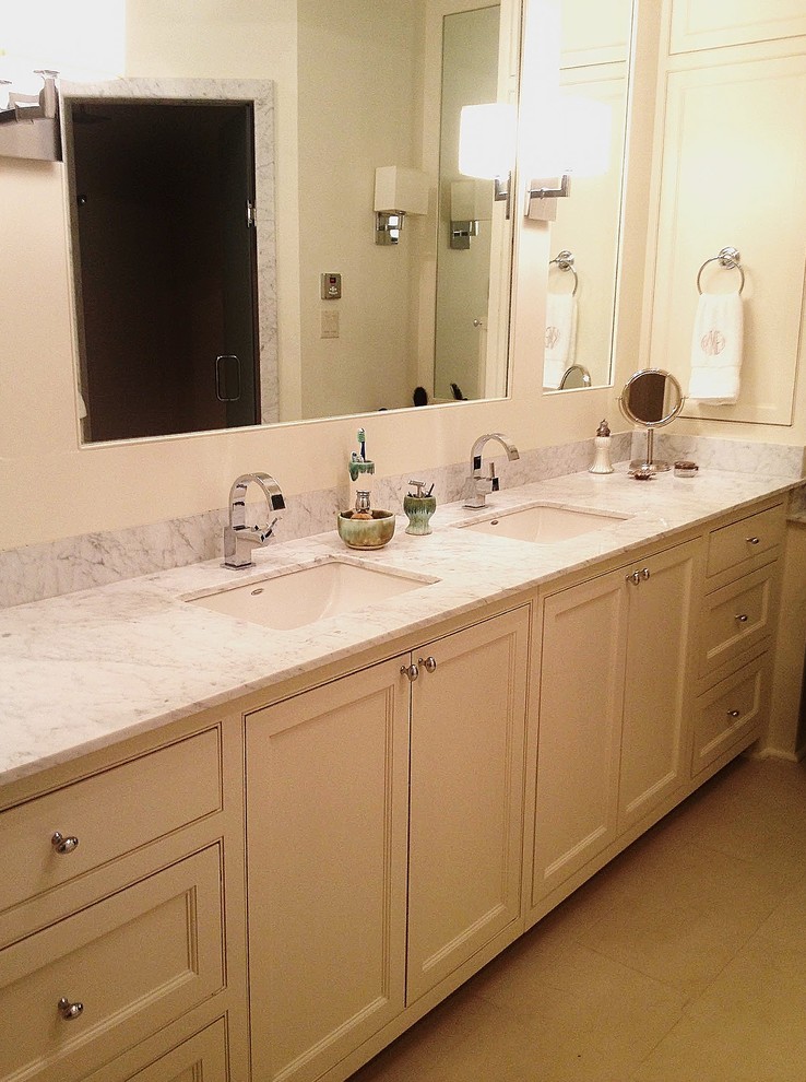 Cette image montre une salle de bain design de taille moyenne avec un lavabo encastré, un placard à porte shaker, des portes de placard blanches, un plan de toilette en marbre, des carreaux de céramique, un mur blanc et un sol en travertin.