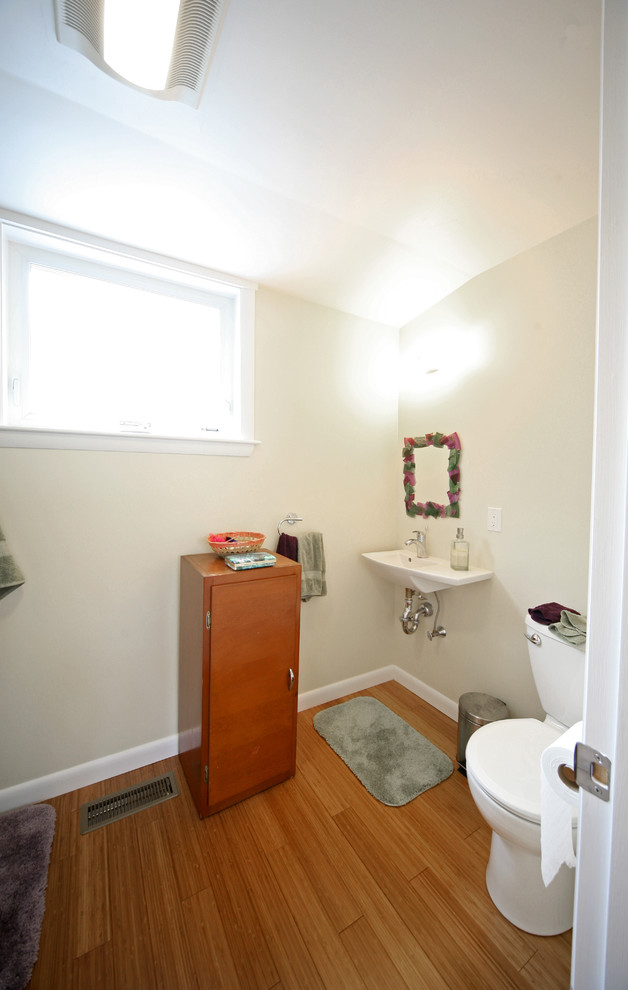 Cette image montre une salle de bain traditionnelle avec un placard à porte plane, des portes de placard marrons, une baignoire en alcôve, un combiné douche/baignoire, WC séparés, un mur vert, parquet en bambou et un lavabo suspendu.