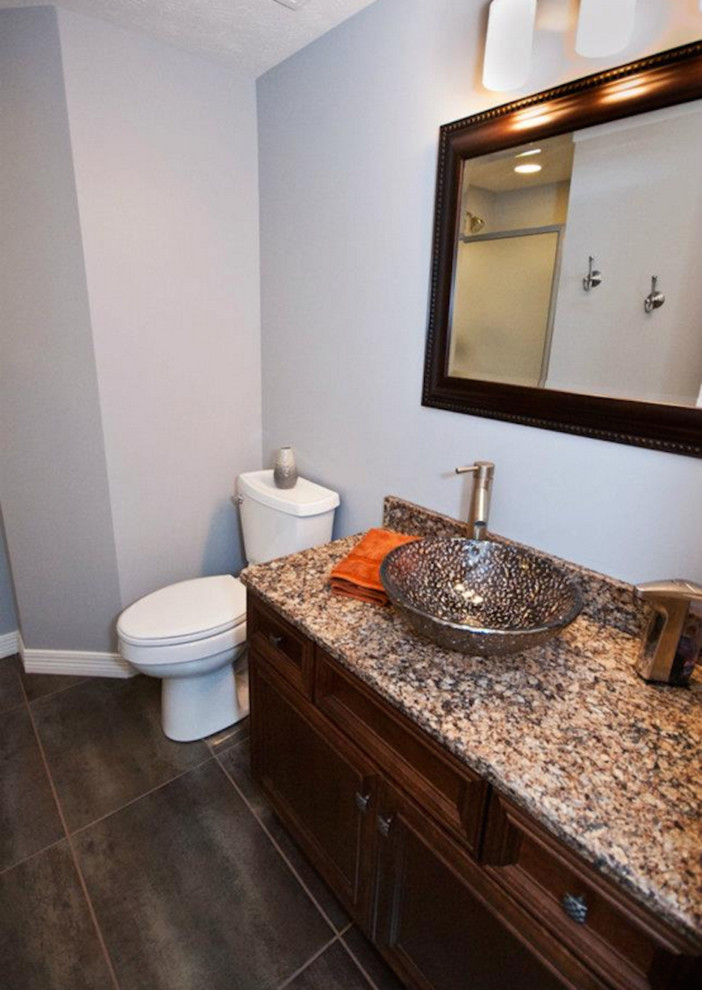 Klassisk inredning av ett badrum, med ett fristående handfat, luckor med profilerade fronter, skåp i mörkt trä, granitbänkskiva, en toalettstol med hel cisternkåpa, blå väggar och klinkergolv i porslin
