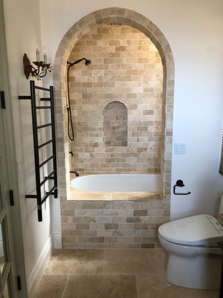 На фото: большая главная ванная комната в средиземноморском стиле с полновстраиваемой ванной, душем над ванной, унитазом-моноблоком, бежевой плиткой, плиткой из известняка, бежевыми стенами, полом из известняка, бежевым полом и открытым душем с