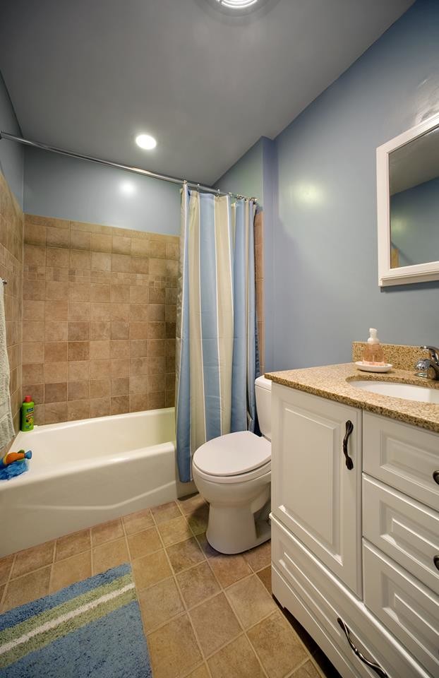 Example of a mid-sized brown tile and ceramic tile ceramic tile alcove shower design in New York with raised-panel cabinets, white cabinets, granite countertops, a one-piece toilet and blue walls