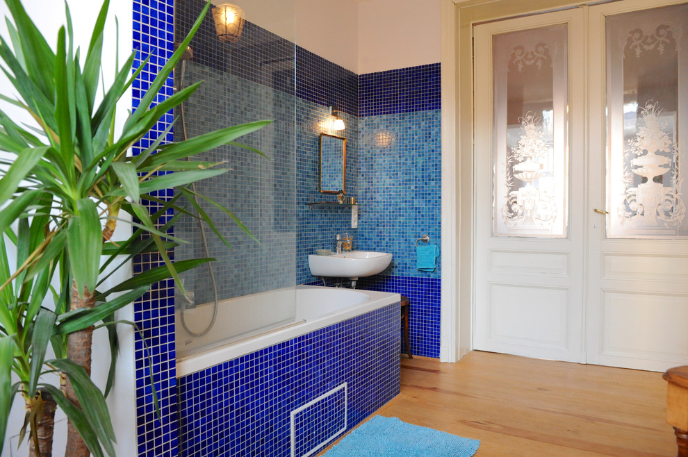 Пример оригинального дизайна: главная ванная комната в стиле неоклассика (современная классика) с угловой ванной, душем над ванной, синей плиткой, светлым паркетным полом, подвесной раковиной и открытым душем