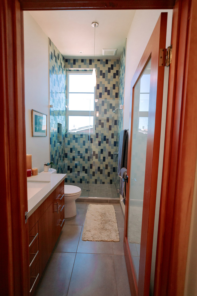 サンフランシスコにある高級な中くらいなエクレクティックスタイルのおしゃれなバスルーム (浴槽なし) (フラットパネル扉のキャビネット、中間色木目調キャビネット、一体型トイレ	、緑のタイル、セラミックタイル、白い壁、セラミックタイルの床、アンダーカウンター洗面器、珪岩の洗面台、マルチカラーの床、開き戸のシャワー、グレーの洗面カウンター) の写真