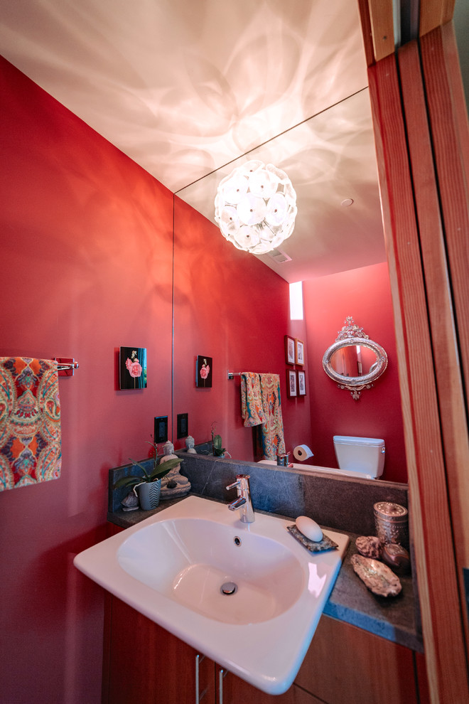 Modelo de cuarto de baño bohemio pequeño con armarios con paneles lisos, puertas de armario de madera oscura, sanitario de una pieza, paredes rojas, suelo de madera clara, encimera de esteatita, suelo beige y encimeras grises