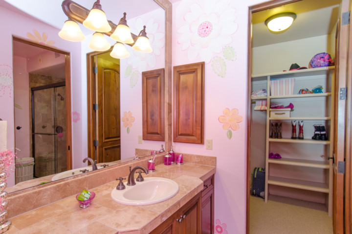 Ispirazione per una stanza da bagno per bambini classica con lavabo da incasso, ante con bugna sagomata, ante in legno scuro, piastrelle beige, piastrelle in pietra, pareti rosa e pavimento in marmo