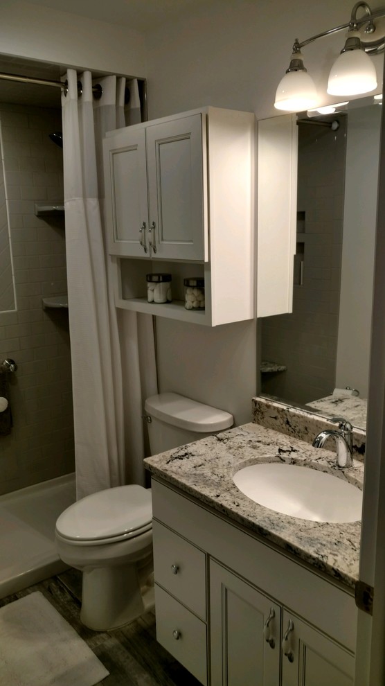 Photo of a medium sized traditional ensuite bathroom in Other with recessed-panel cabinets, white cabinets, an alcove shower, a two-piece toilet, grey tiles, metro tiles, white walls, laminate floors, a submerged sink, granite worktops, grey floors and a shower curtain.
